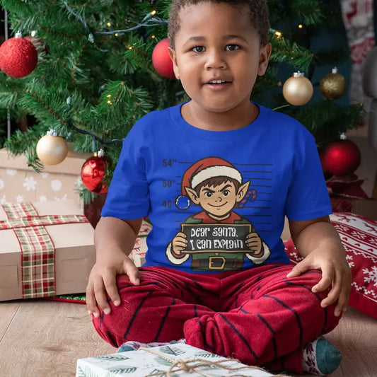 Child sitting by a Christmas tree in a True Royal blue Dear Santa I Can Explain kids elf t-shirt