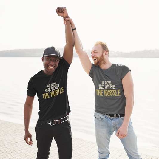 Two graduates wearing The Tassel Was Worth The Hustle tees celebrating at waterfront — streetwear graduation gift
